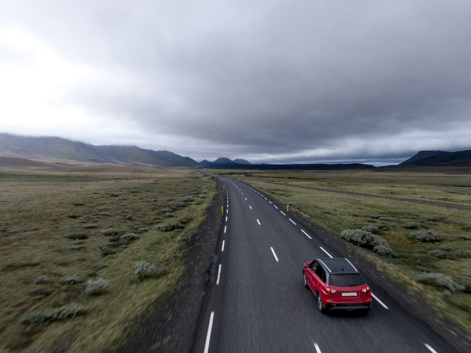 Red car travelling along an open road through a mountain landscape